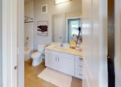 Thumbnail 12 of 43 - A clean bathroom here at Experience at Epicenter featuring light tile flooring, a white vanity with a smooth countertop, and a wide mirror beneath modern wall lighting. A toilet sits beside a bathtub with white subway tile surround, while neutral walls, simple décor, and a soft bath mat create a bright, tidy, and welcoming space.