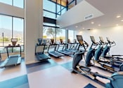 Thumbnail 32 of 43 - A modern fitness center here at Experience at Epicenter featuring rows of cardio equipment, including treadmills and elliptical machines, arranged on sleek flooring beneath high ceilings. Floor-to-ceiling windows fill the space with natural light and showcase mountain views, creating an open, energizing environment for workouts.
