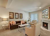 Thumbnail 1 of 32 - A cozy living room here at Windsong featuring a warm brown sofa with orange accent pillows, beige armchairs, and a sleek mirrored fireplace. Bright, inviting space with soft carpet, elegant side tables, and welcoming natural light.