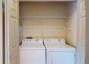 Thumbnail 16 of 32 - A laundry area here at Windsong featuring full-size washer and dryer units, open shelving for storage, and a clean, organized layout. Bright finishes and convenient design make everyday laundry simple and efficient.