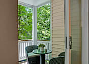 Thumbnail 17 of 32 - A private balcony here at Windsong featuring a cozy bistro table with two woven chairs, surrounded by lush green tree views. Bright and peaceful, this inviting outdoor space is perfect for relaxing or enjoying fresh air.