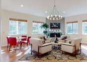 Thumbnail 19 of 32 - A resident lounge here at Windsong featuring bright windows, cozy armchairs, and a fireplace with mounted TV. Warm and welcoming, this stylish space includes a patterned rug, round chandelier, and inviting seating areas perfect for relaxing or gathering.