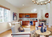 Thumbnail 20 of 32 - A resident lounge here at Windsong featuring cozy armchairs, a round coffee table, and a kitchenette with warm wood cabinets. Bright and welcoming, this stylish space offers high ceilings, large windows, and comfortable seating perfect for relaxing or socializing.