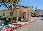 Thumbnail 30 of 32 - A leasing office exterior here at Windsong featuring a welcoming covered entrance, clean siding, landscaped greenery, and a curved driveway, creating an inviting and well-maintained community arrival experience.
