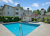 Thumbnail 21 of 32 - A sparkling outdoor pool here at Windsong surrounded by charming apartment buildings and lush greenery. This bright and inviting space offers clear blue water, a relaxing hot tub, and a peaceful setting perfect for enjoying sunny days.
