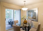 Thumbnail 7 of 32 - A bright dining area here at Windsong featuring a glass table, beige upholstered chairs, and an amber centerpiece vase. Welcoming layout with sliding door access to a private balcony and soft, natural light.