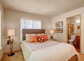 Thumbnail 8 of 32 - A cozy bedroom here at Windsong featuring a tufted headboard bed, orange accent pillows, and matching bedside lamps. Bright, welcoming layout with soft carpet, neutral tones, and convenient ensuite bathroom access.