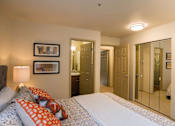 Thumbnail 10 of 32 - A welcoming bedroom here at Windsong featuring mirrored closet doors, soft carpet, and bright neutral walls. Cozy bed with patterned bedding and orange accent pillows adds warmth, while open doorways provide convenient access to bathroom and storage areas.