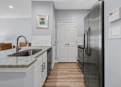 Thumbnail 23 of 42 - A modern kitchen with a stainless steel refrigerator and a white sink.