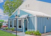 Thumbnail 6 of 11 - A blue house with a white roof and a red car parked in front.