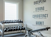 Thumbnail 7 of 11 - A gym wall with a bench and weights and a motivational poster.