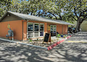 Thumbnail 6 of 7 - A small building with a brown roof and a signboard in front.