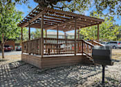Thumbnail 2 of 7 - A wooden gazebo with a roof and a bench is situated in a gravel area.