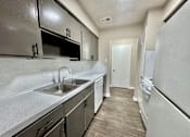 Thumbnail 1 of 13 - Modern kitchen at Greenbriar Place 55+ Apartments in Corpus Christi featuring white cabinets, stainless steel sink, and full-size refrigerator.