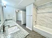 Thumbnail 10 of 25 - A bathroom with a marble countertop and a white bathtub.