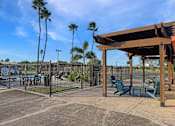 Thumbnail 4 of 15 - A wooden pergola is in the middle of a patio with chairs and a table.