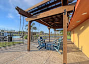 Thumbnail 10 of 15 - A wooden pergola with blue benches is in the foreground of a sunny day.