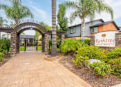Thumbnail 1 of 36 - A brick pathway leads to a gate with an archway and a sign that says Raintree Apartments at Raintree Apartments, CA 92346