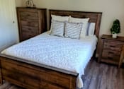 Thumbnail 13 of 36 - A bedroom with a large bed and a small tree on the nightstand at Raintree Apartments, CA 92346