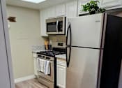Thumbnail 7 of 36 - A black refrigerator stands in a kitchen with a stove and microwave in the background at Raintree Apartments, CA 92346