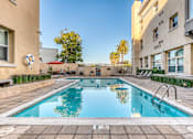 Thumbnail 9 of 20 - a swimming pool with a yellow building and palm trees in the background
