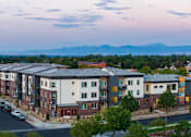 Thumbnail 1 of 24 - A street view of a residential area with apartment buildings and cars parked on the side of the road.