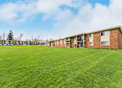 Thumbnail 21 of 21 - A grassy field in front of a brick building with cars parked in the background at Integrity Chardon Apartments,Ohio, 44024