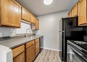 Thumbnail 12 of 21 - A kitchen with wooden cabinets and a black refrigerator at Integrity Chardon Apartments,Ohio