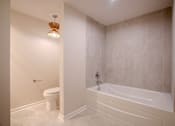 Thumbnail 32 of 42 - A white bathroom with a toilet, tub, and a light fixture t Atrium in The Village, Beachwood