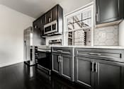Thumbnail 17 of 23 - A black and white kitchen with a stainless steel refrigerator and oven.