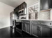 Thumbnail 15 of 29 - A black and white kitchen with a refrigerator, oven, and microwave.