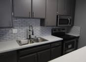 Thumbnail 7 of 21 - White tiled kitchen with stainless steel fridge, microwave, and oven.