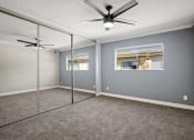 Thumbnail 9 of 15 - Carpeted bedroom with ceiling fan and large mirrored closet.