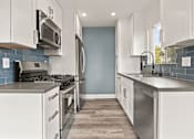 Thumbnail 2 of 15 - Blue tiled kitchen with stainless steel oven, microwave, and fridge.