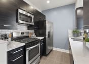 Thumbnail 8 of 22 - White tile kitchen with granite countertop and stainless steel fridge, oven, and fixtures.