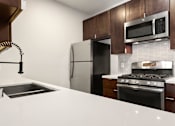 Thumbnail 5 of 23 - White tiled kitchen with modern faucet, stainless steel appliances, and refrigerator.