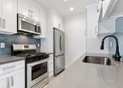 Thumbnail 1 of 22 - Blue tiled kitchen with quartz stone counters and stainless steel microwave, oven, fridge, and fixtures.
