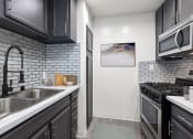Thumbnail 2 of 20 - White tiled kitchen with stainless steel fridge, oven, microwave, and fixtures.