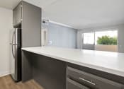 Thumbnail 6 of 21 - White tiled kitchen with bar seating facing hardwood floored living room.