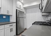 Thumbnail 5 of 19 - Blue tiled kitchen with stainless steel oven, fridge, and fixtures.