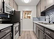 Thumbnail 3 of 22 - White tiled kitchen with stainless steel oven, microwave, and fridge..
