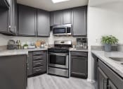 Thumbnail 3 of 20 - Stone tiled kitchen with stainless steel oven, microwave, and fixtures.