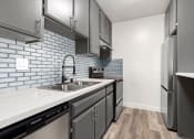 Thumbnail 2 of 21 - White tiled kitchen with stainless steel fridge, microwave, and oven.