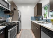 Thumbnail 5 of 22 - Blue tiled kitchen with granite countertop and stainless steel fridge, microwave, and fixtures.