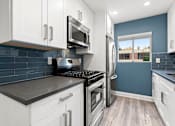 Thumbnail 8 of 31 - Blue tiled kitchen with stainless steel fridge, oven, and microwave.