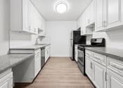 Thumbnail 7 of 24 - Large white tiled kitchen with stainless steel oven, microwave, and fridge.