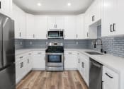 Thumbnail 2 of 27 - White tiled kitchen with stainless steel fridge, over, microwave, and fixtures.