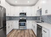 Thumbnail 2 of 24 - White tiled kitchen with stainless steel fridge, over, microwave, and fixtures.