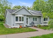 Thumbnail 2 of 27 - A house with a grey siding and a white door is surrounded by greenery.