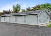 Thumbnail 5 of 27 - A long garage with four doors is surrounded by a driveway and a grassy area.
